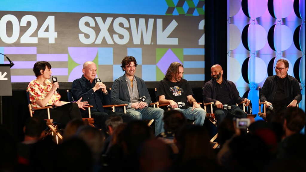 Actors seated on stage speaking into microphones.