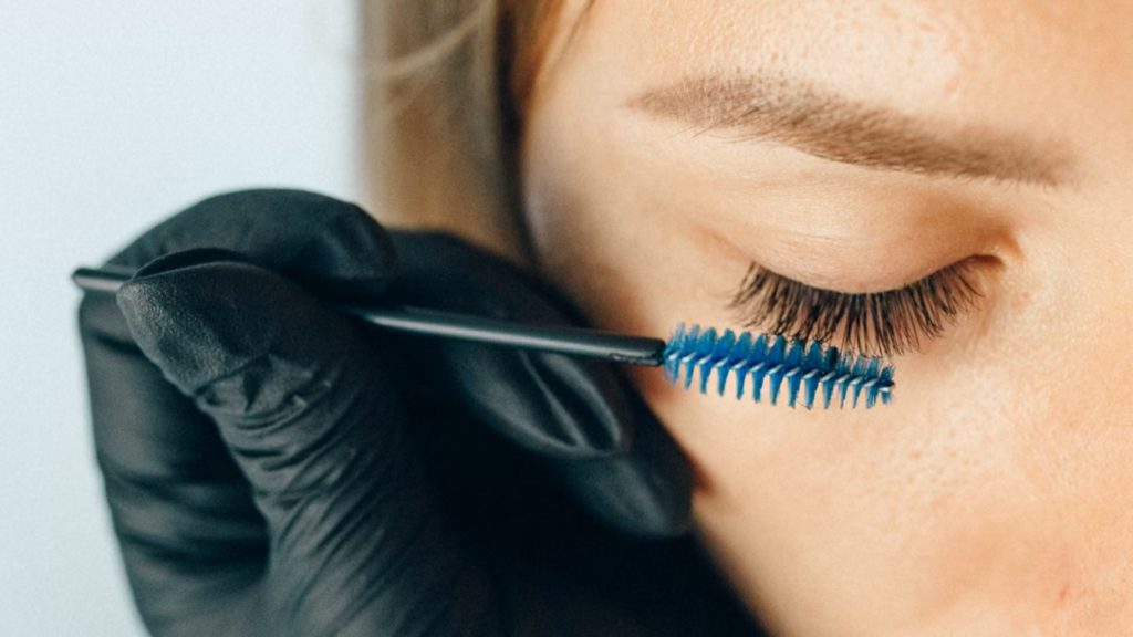 Brushing eyelash extensions using a blue spoolie brush.