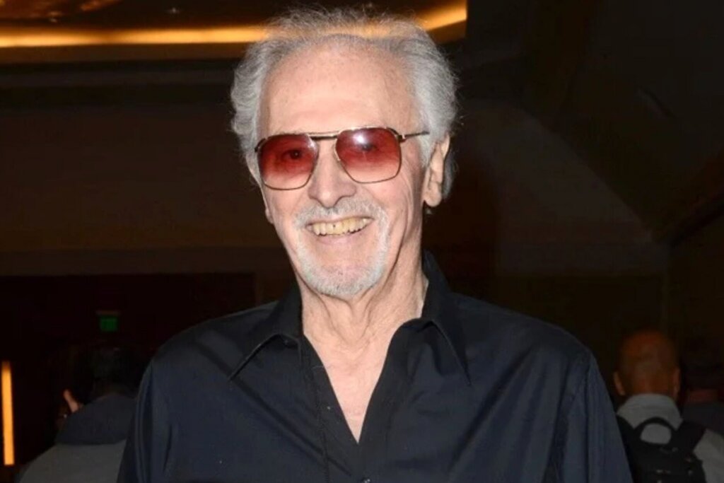 Michael Forest smiling in a black shirt and red-tinted sunglasses at an event.