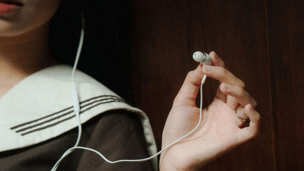 Person holding up a white wired earbud.