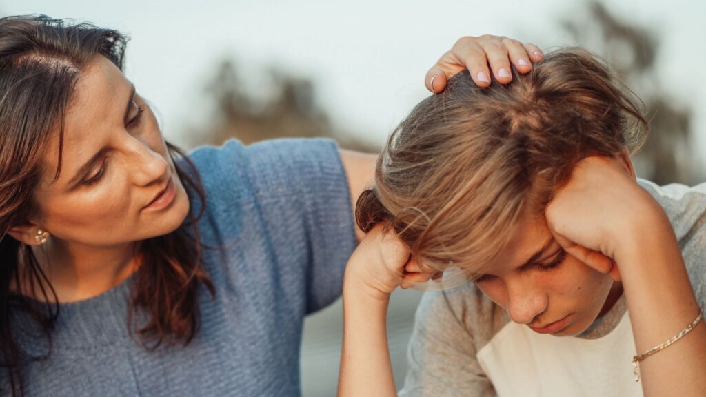 Woman comforting teenager resting head in hands.