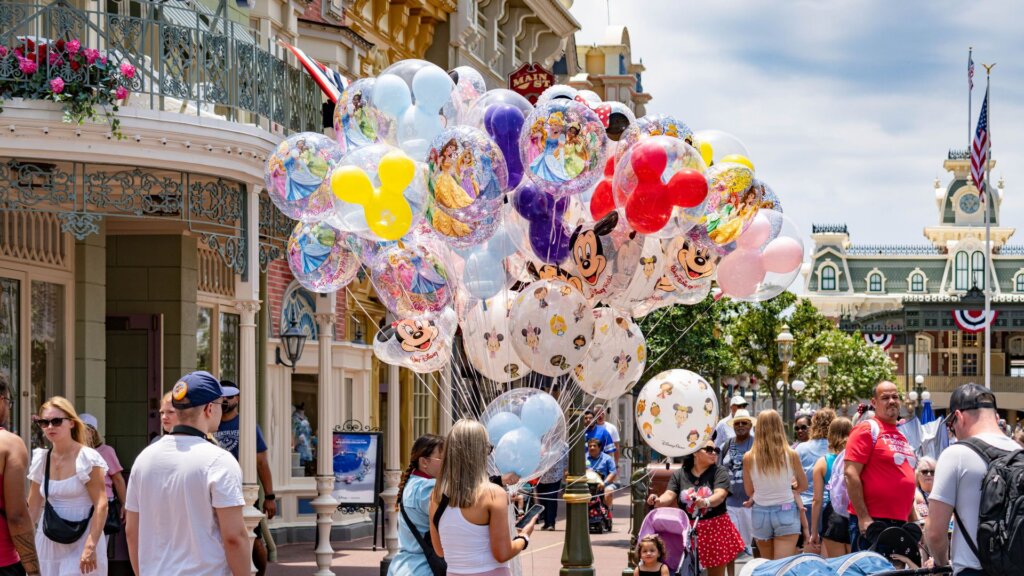 Crowd of visitors on Main Street, U.S.A. walking past a large bunch of Mickey-shaped and princess balloons.