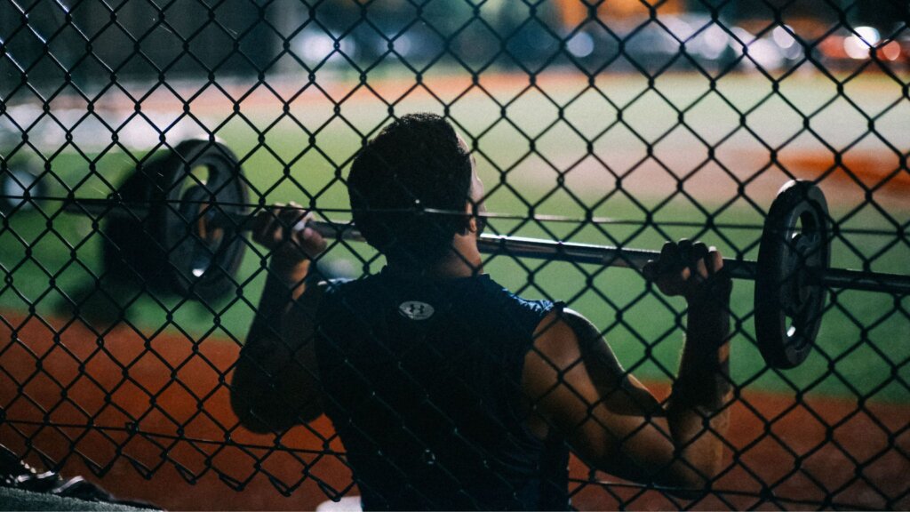 Person lifting barbell behind chain link fence at night.