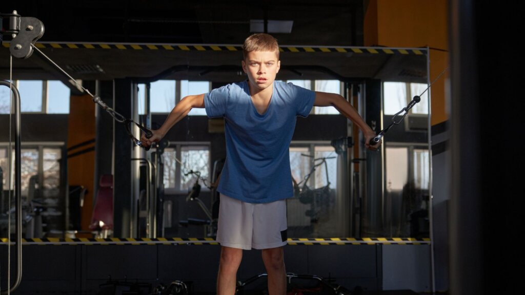 Boy doing cable machine exercise in dim gym.