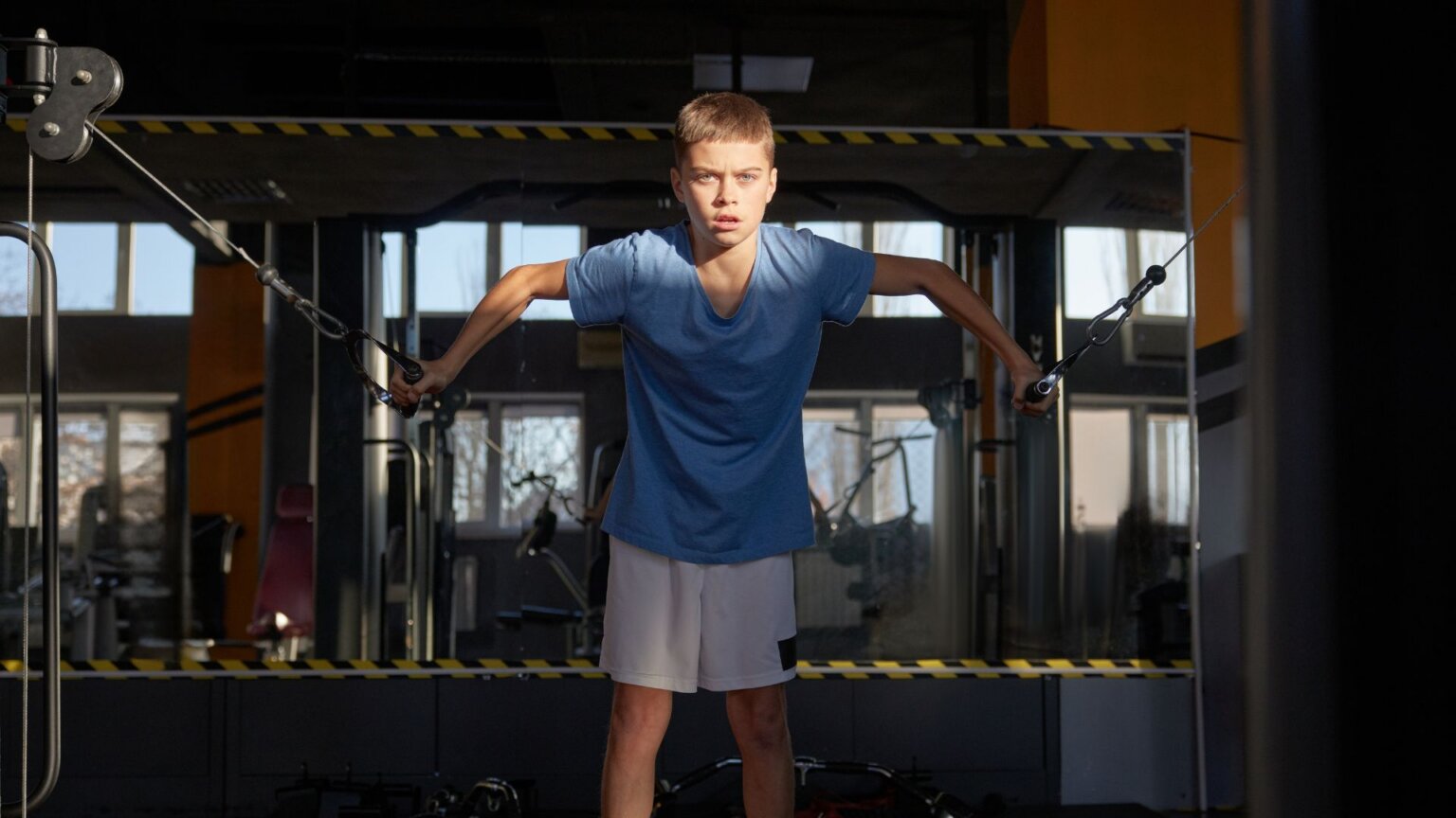 Boy doing cable machine exercise in dim gym.