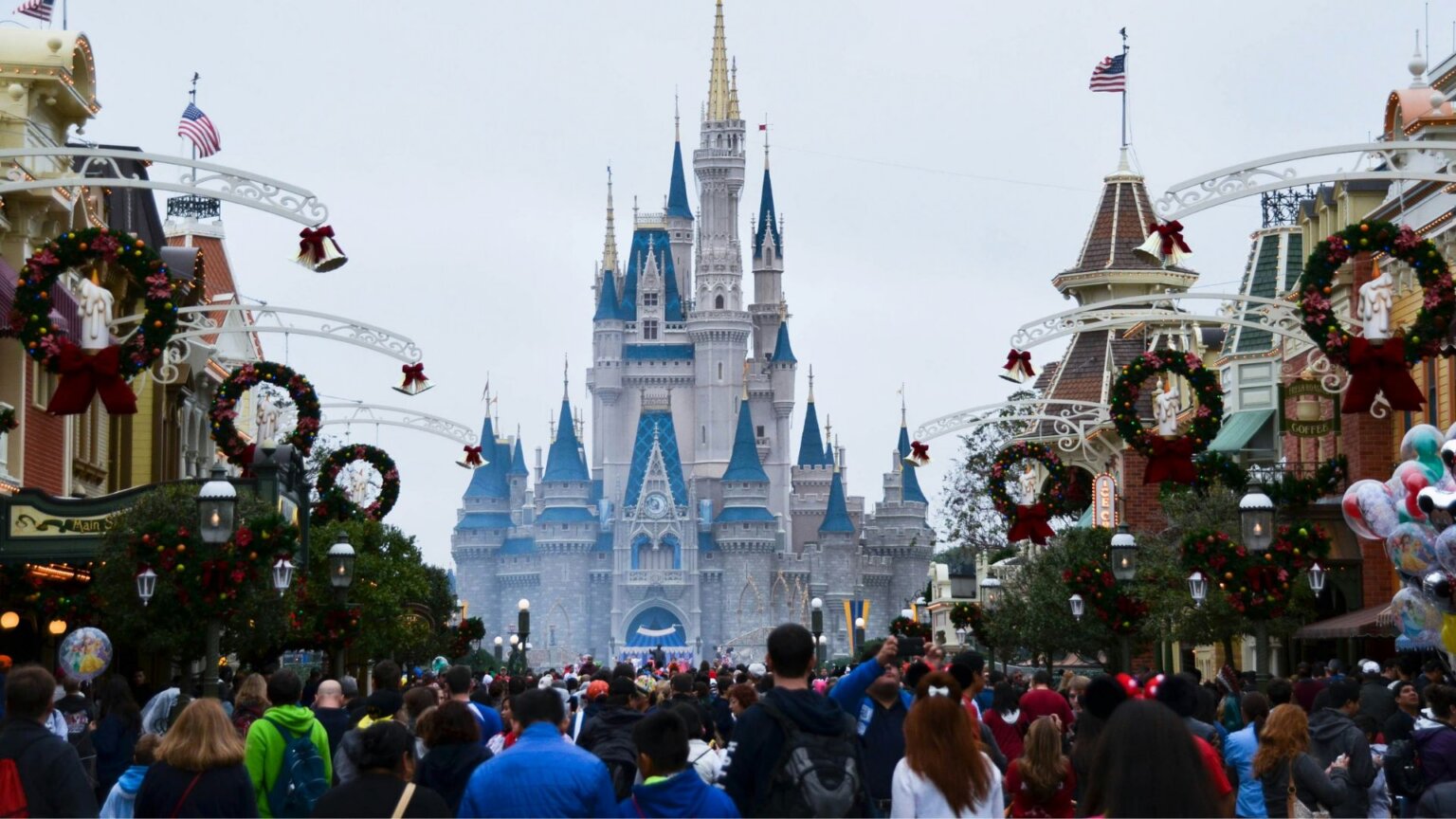 Crowd on Main Street, U.S.A. facing Cinderella Castle, with holiday wreaths hanging along both sides,