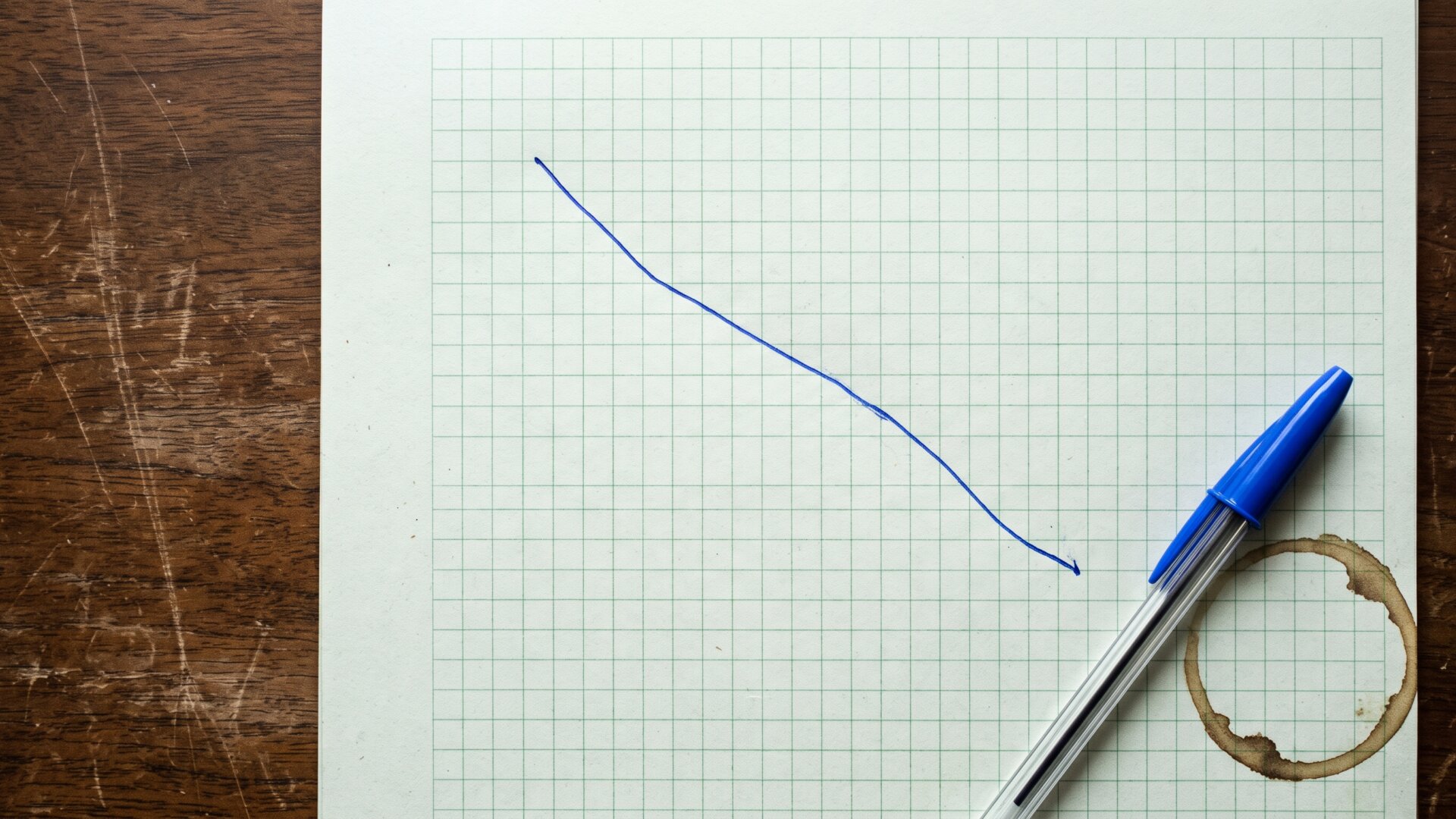 A printed price chart lying on a desk with the line falling, kept abstract and unlabeled, matching slide 7's point about markets pricing uncertainty.