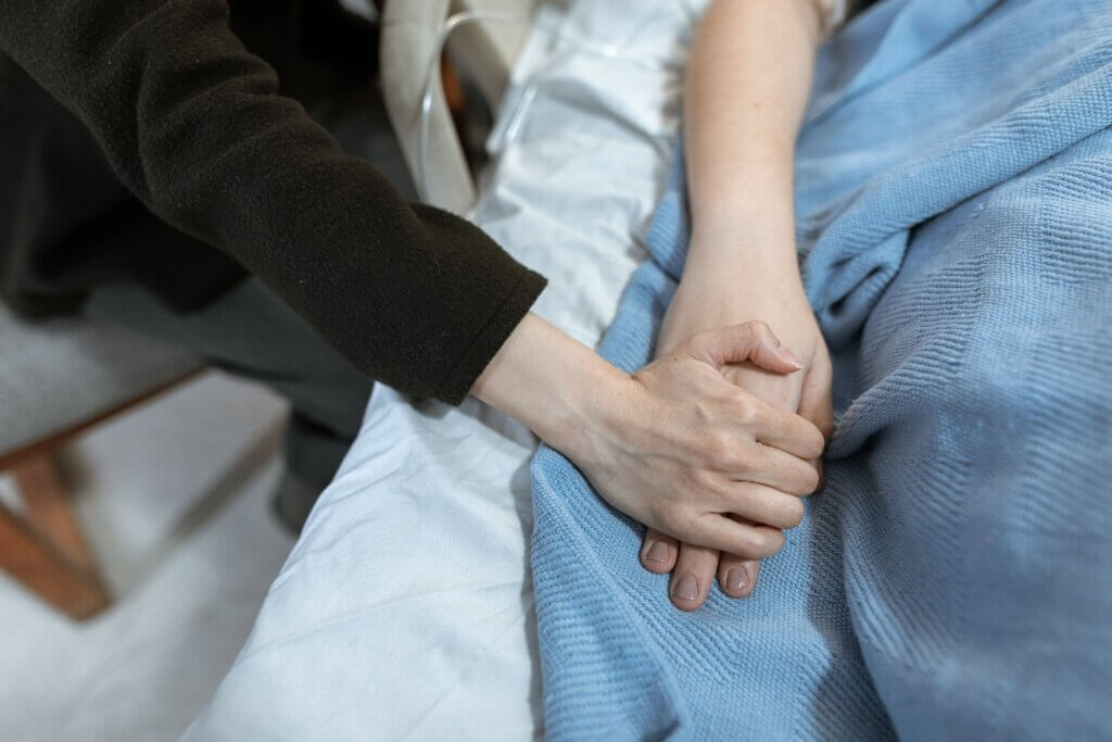 Person holding a hospital patient's hand at the bedside in a gesture of support.