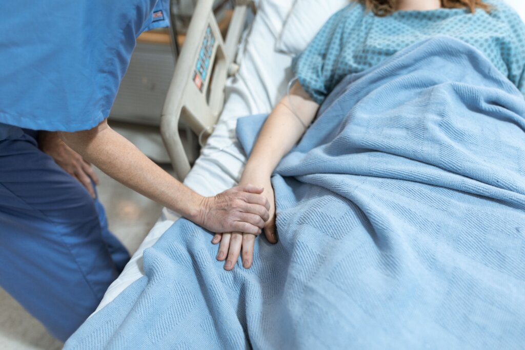 Nurse holding a patient's hand beside a hospital bed, offering comfort and reassurance during medical care.
