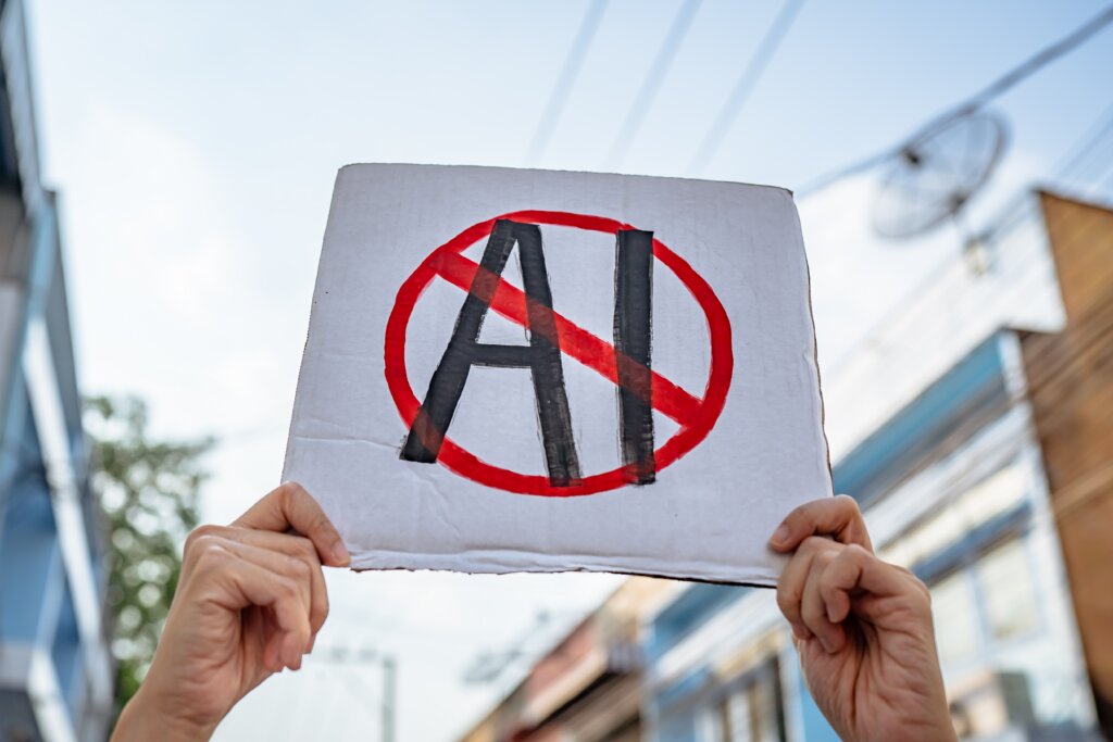 Hands holding a protest sign featuring the letters “AI” crossed out with a red prohibition symbol.
