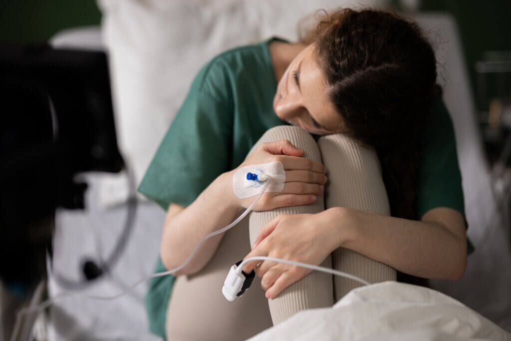 Hospital patient with an IV line sitting on a bed and embracing their knees.