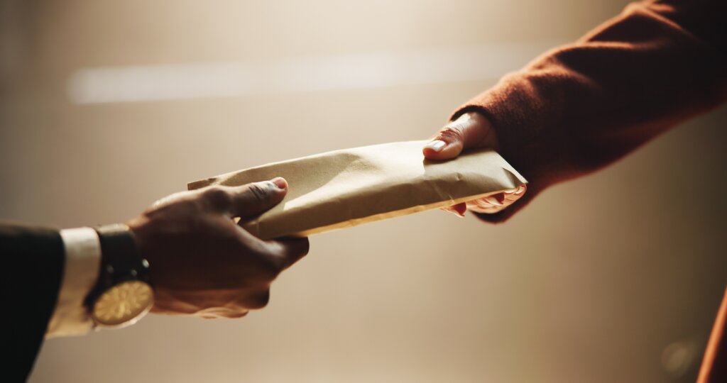 Two people exchanging a sealed envelope, illustrating concerns about suspicious financial transactions and money laundering.