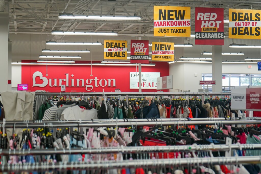 Clothing racks inside a Burlington store, with colorful signs advertising markdowns, clearance sales, and deals.