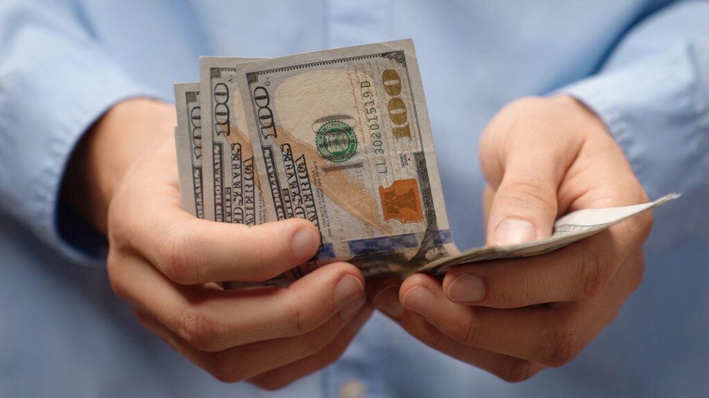 Close-up of a person counting U.S. $100 bills, illustrating potential cash payments from the Zumba class-action settlement.